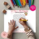 Valentine's Day maze activity sheet with a child's hand holding a pencil, surrounded by colored pencils and blocks.